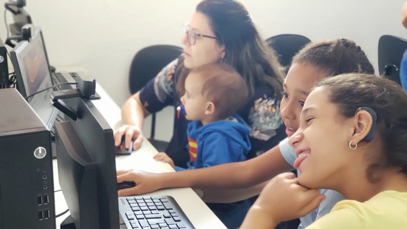 Educadora, mãe com bebê e duas meninas usando o computador no laboratório da AADAS
